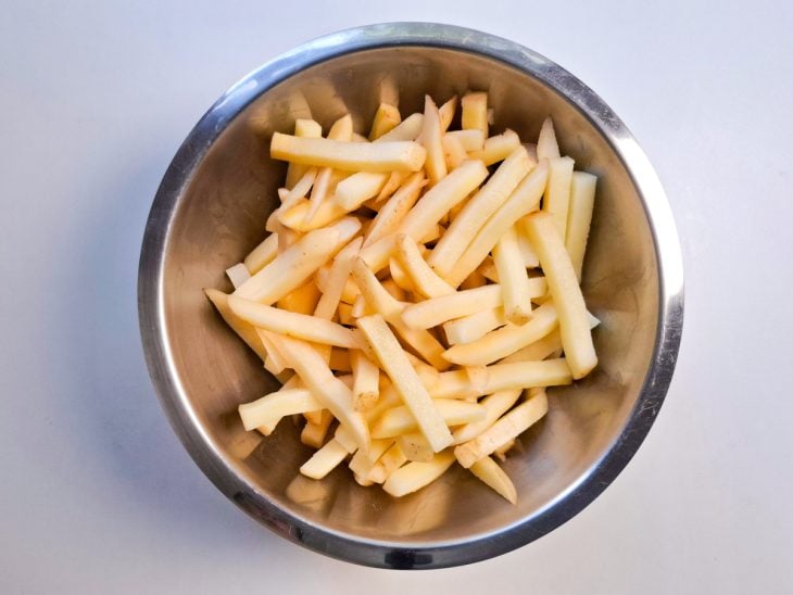Batatas cortas em palitos dentro de um recipiente de alumínio.