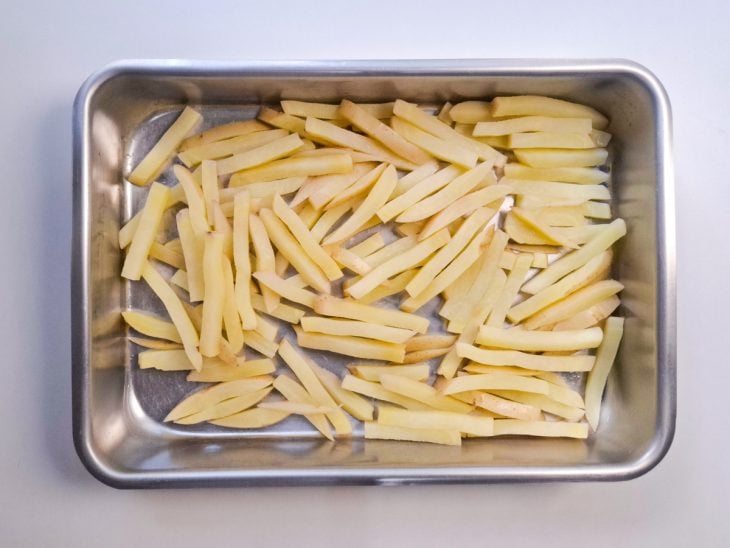 Batatas-palito cozidas e reservadas em uma forma de alumínio.