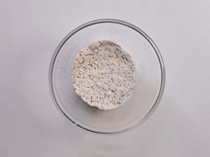Sal, lemon pepper, amido de milho e cebola em pó misturados em um recipiente de vidro.