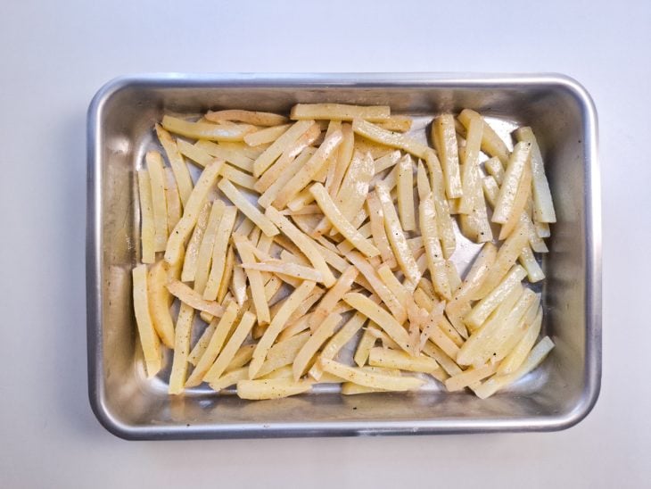 Azeite e mistura de temperos espalhados sobre as batatas que estão na forma.