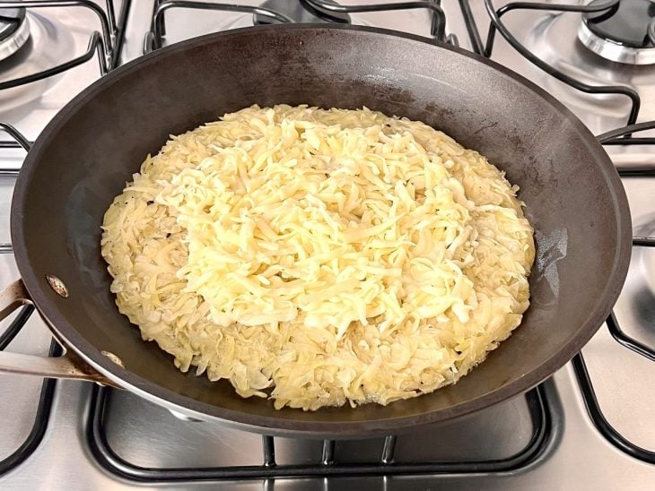 Uma frigideira contendo batatas e queijo ralados.