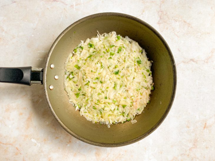 Porção da batata ralada temperada adicionada a uma frigideira com azeite.