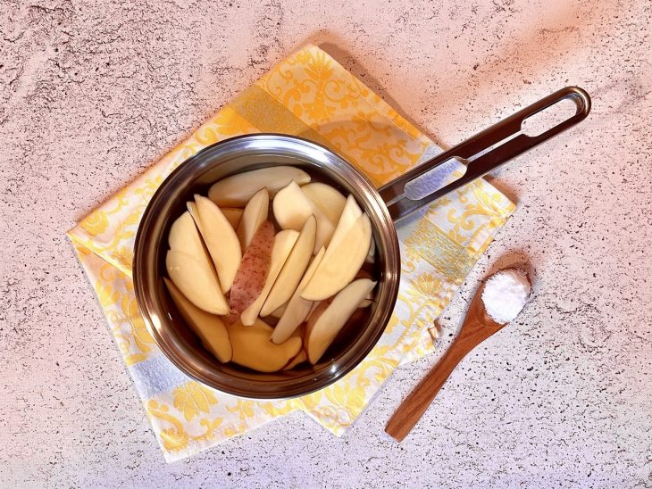 Batatas cortadas no formato canoa em uma panela com água.