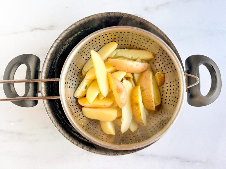 Batatas sendo fervidas em panela com água, sal e bicarbonato.