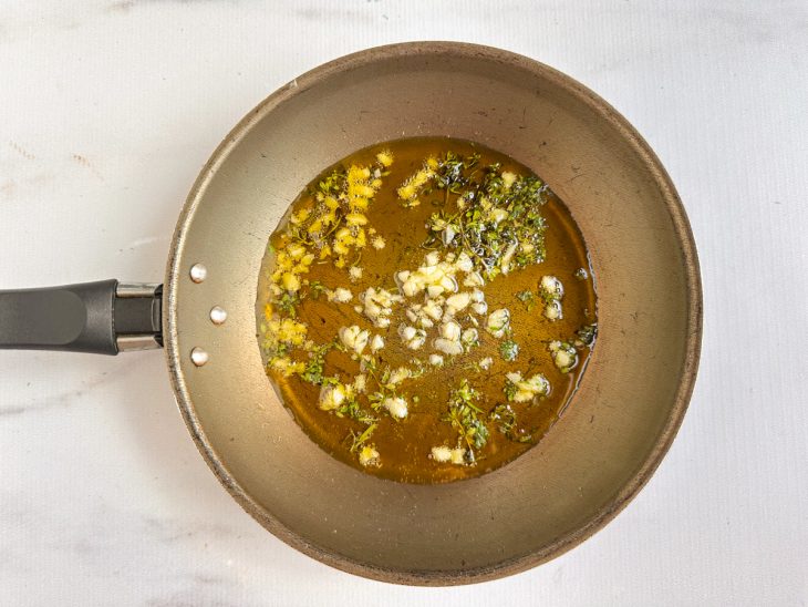 Azeite sendo aquecido com alho e ervas frescas.