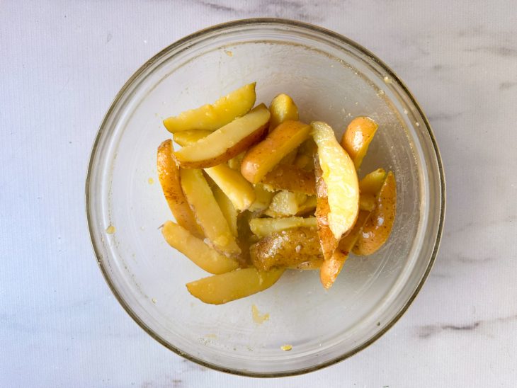 Batatas envolvidas com o azeite aromatizado em uma tigela.