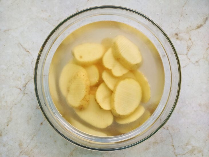 Batatas cortadas de molho em tigela com água e sal.