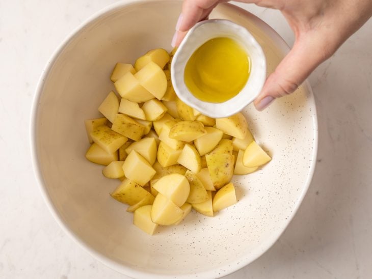 Azeite sendo despejado sobre a tigela com as batatas.
