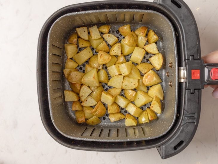 Air fryer com batatas levemente douradas.