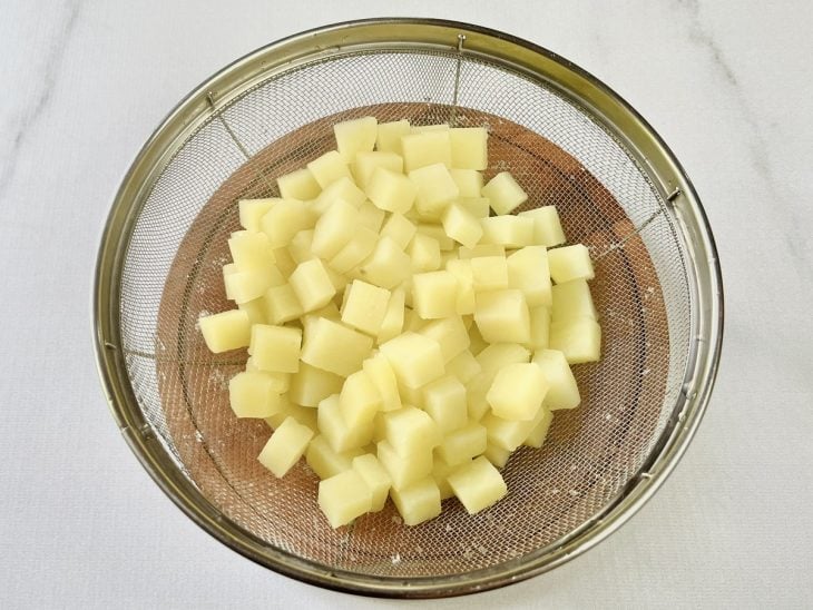 Uma peneira com batatas escorridas.