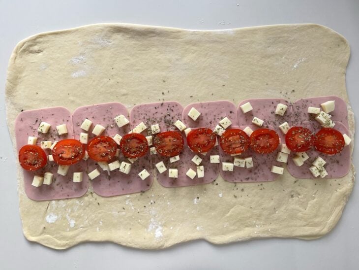 Rodelas de tomate alinhadas sobre o queijo recebendo uma chuva de orégano seco.
