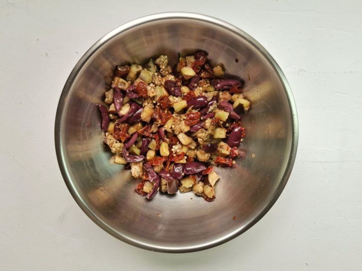 Berinjela misturada em uma tigela com tomate seco e azeitona.