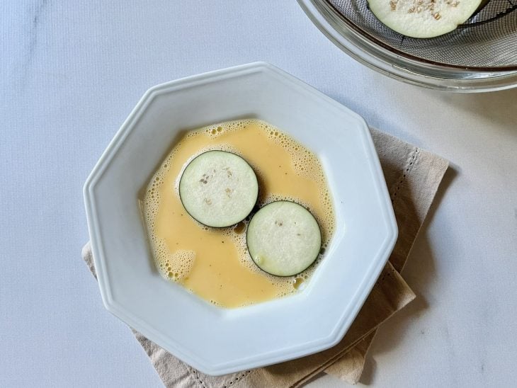 Rodelas de berinjela sendo cobertas com o ovo batido.