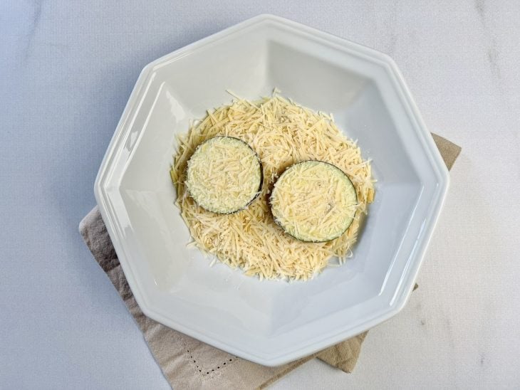 Berinjela sendo empanada no prato com queijo parmesão.