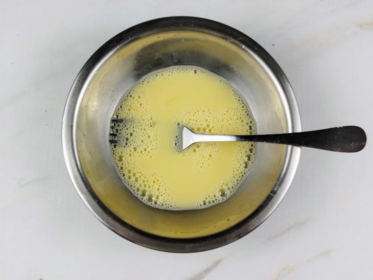 Uma tigela com ovo e leite batidos com um garfo.