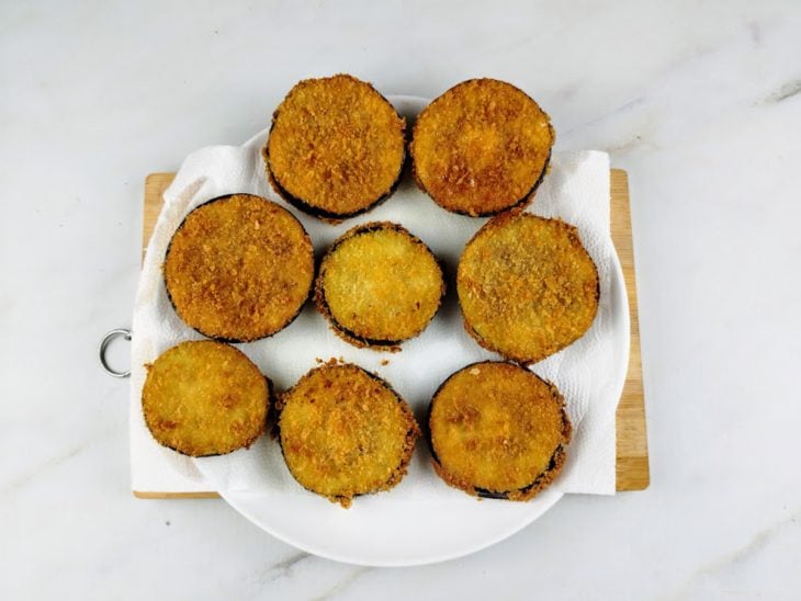 Um prato forrado com papel-toalha e as rodelas de berinjela fritas.