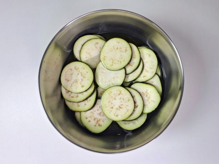 Rodelas de berinjelas em um tigela com água, vinagre e sal.