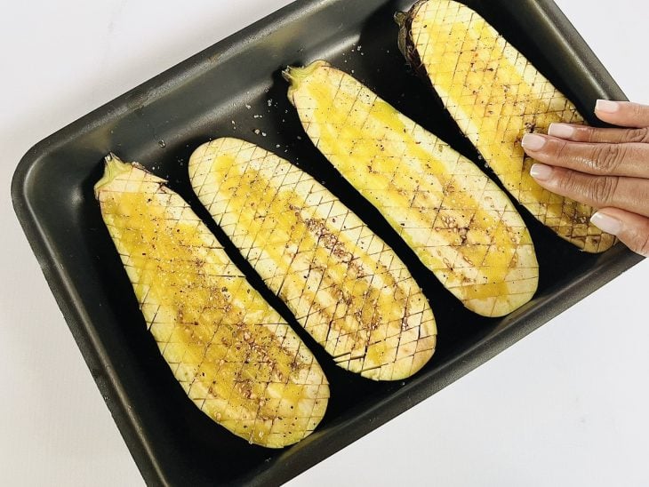 duas berinjelas cortadas ao meio, temperadas com azeite, dentro de uma forma