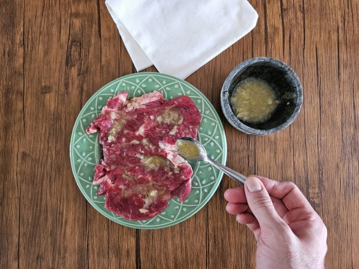 Um prato contendo bifes sendo temperados.