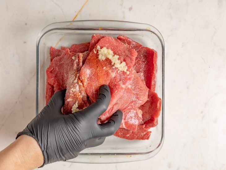 Bifes de patinho sendo temperados em um refratário.