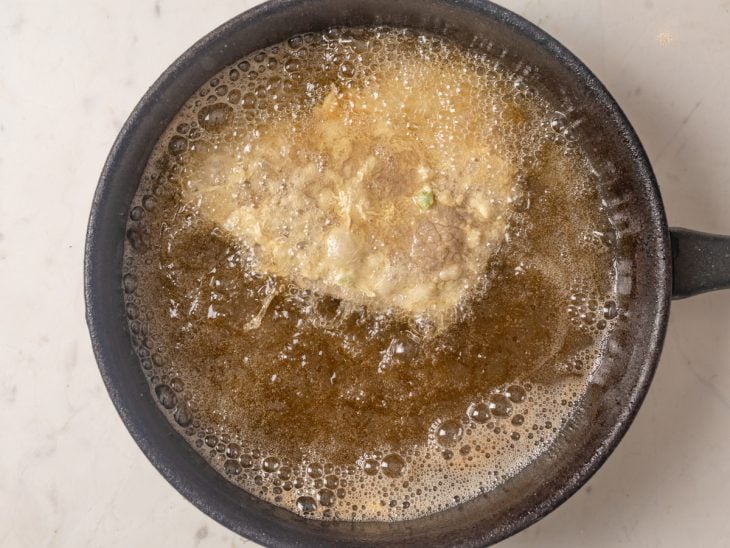 Uma frigideira com óleo quente e um bife fritando.
