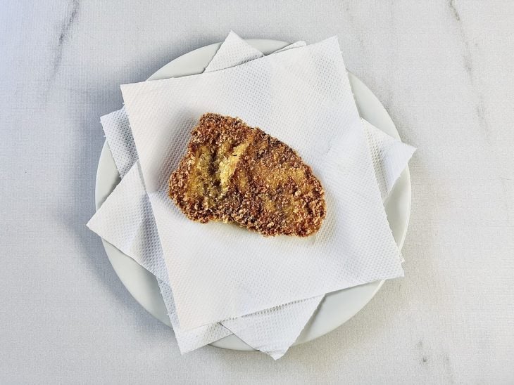 Prato forrado com papel-toalha e bife após fritar.