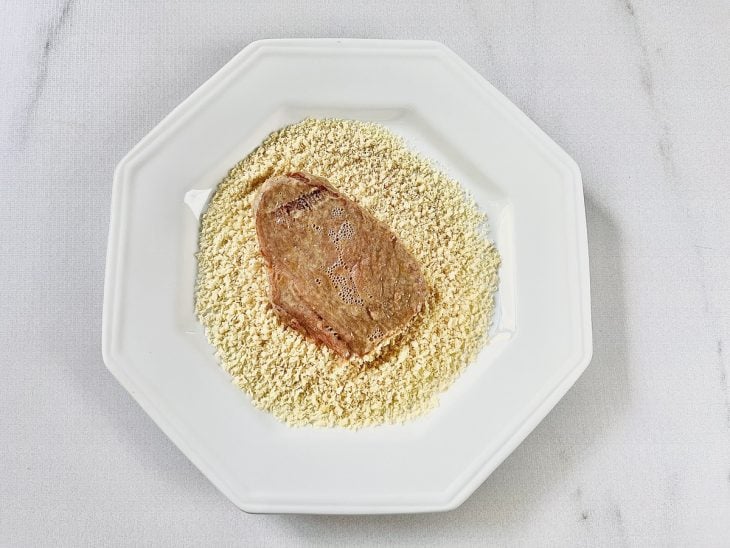 Bife em um prato com farinha de rosca.
