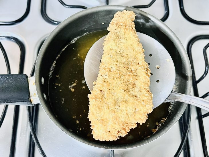 Bife frito sobre uma escumadeira para escorrer o óleo.
