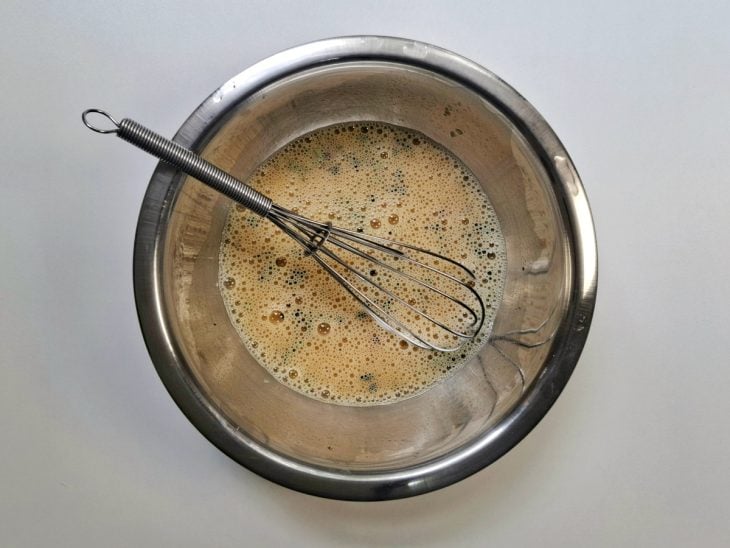 Ingredientes batidos em uma tigela de inox com auxílio de um fouet.