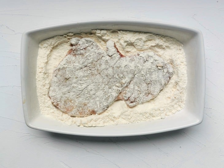 Um recipiente com um bife sendo empanado na farinha de trigo.