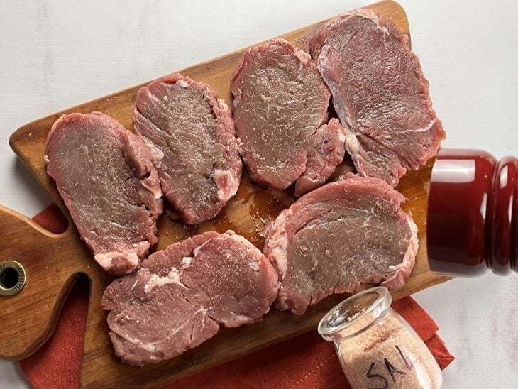 Uma tábua contendo bifes sendo temperados.