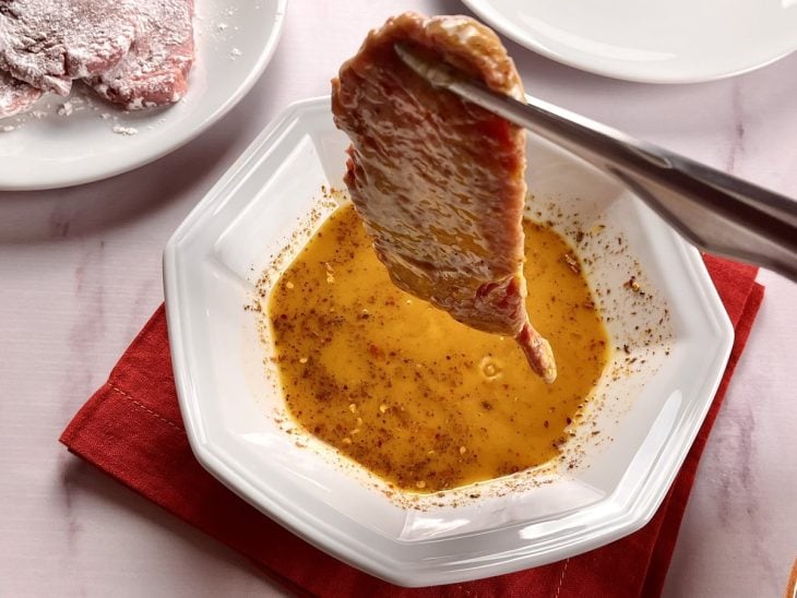 Um bife sendo empanado nos ovos batidos.