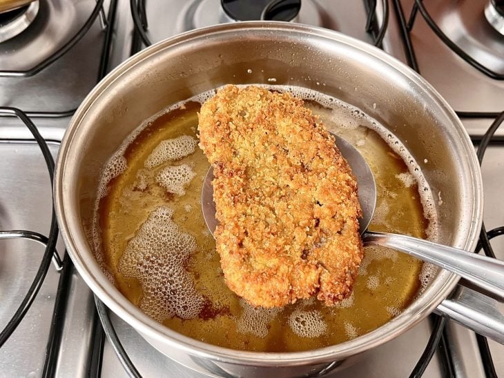 Um bife empanado sendo frito na panela com óleo.