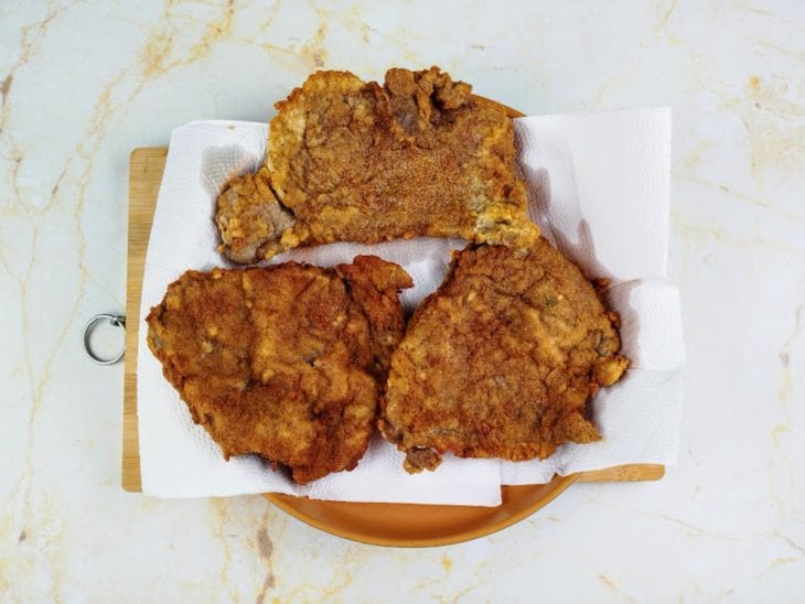Bifes fritos e acomodados sobre um prato com papel-toalha.