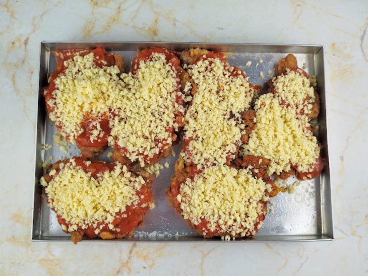 Bifes em uma assadeira com molho de tomate e queijo na superfície.