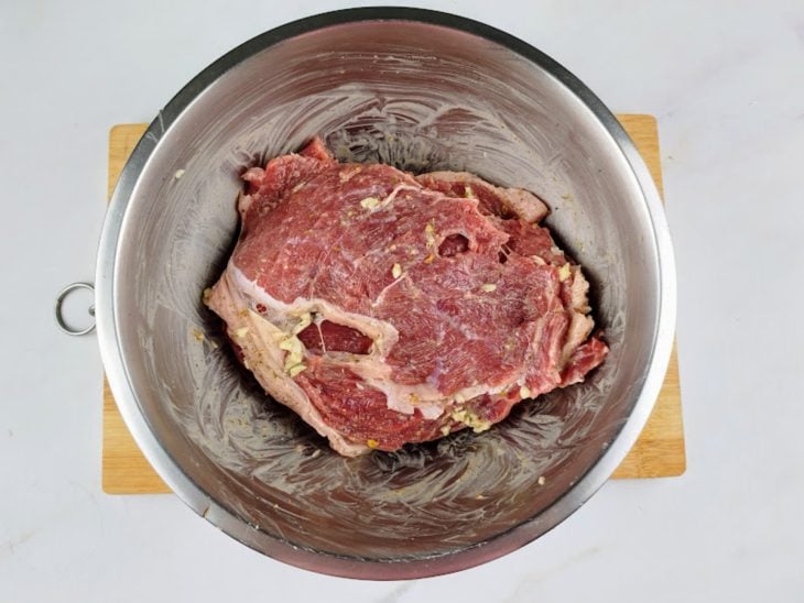 Bifes temperados com sal, pimenta-do-reino, alho amassado, chimichurri e maionese em uma tigela de alumínio.