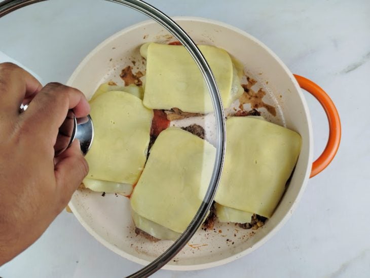 Molho de tomate e queijo mussarela dispostos sobre os bifes na panela.