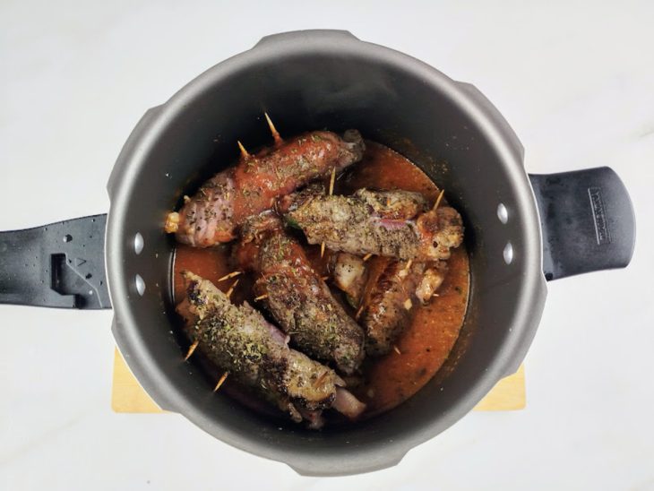 Panela de pressão com os bifes a rolê, molho e temperos.
