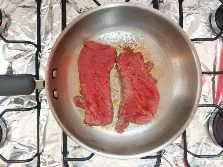 Frigideira com dois bifes dourados de um lado.