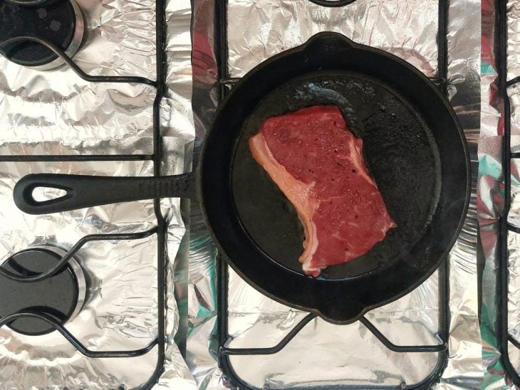 Bife na frigideira no fogão com a aparência ainda crua.