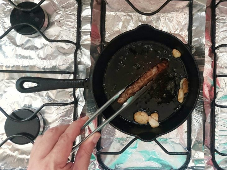 Bife no pegador, sendo segurado de lado na frigideira para fritar a lateral do bife.