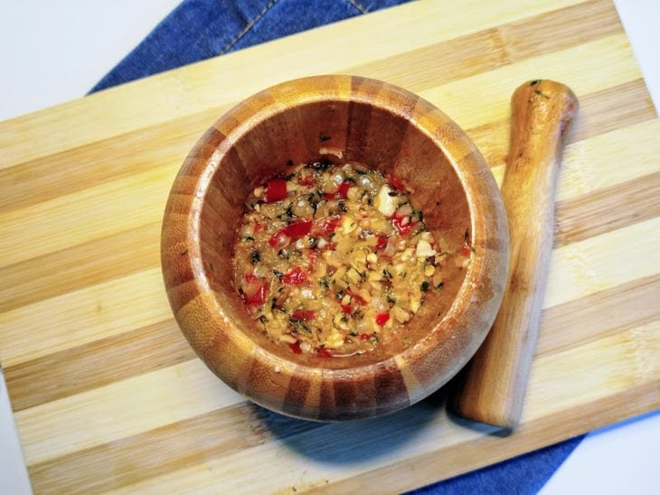 Um pilão contendo pimenta, cebola, alho, tomilho, sal e azeite socados.