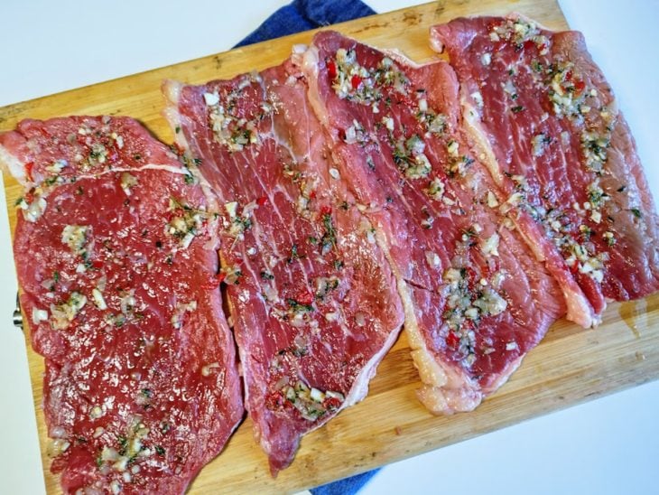 Uma tábua contendo bifes de coxão duro crus e temperados.