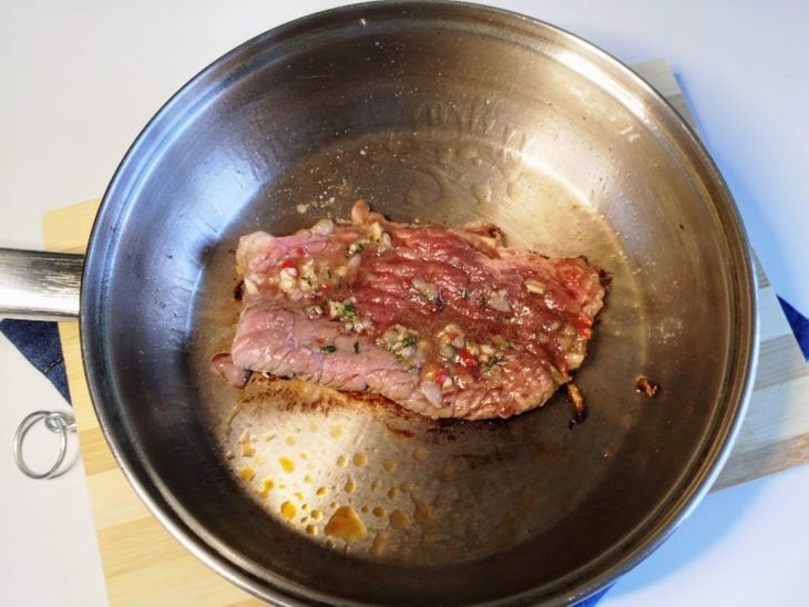 Uma frigideira fritando contendo bife de coxão duro.