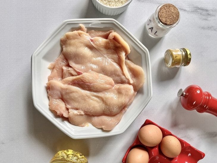 Ingredientes para a receita de bife de frango a milanesa reunidos em uma bancada.