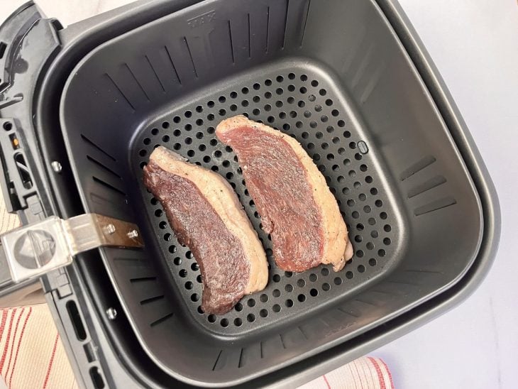 Uma cesta de airfryer com os bifes de picanha dentro.