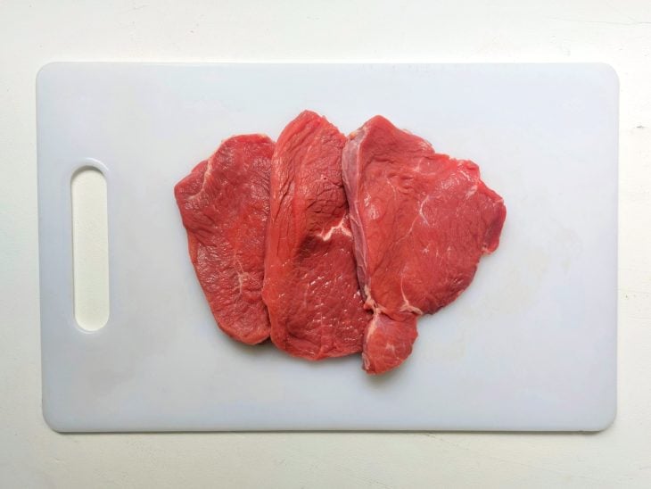 Bifes dispostos em cima de uma tábua de cor branca.