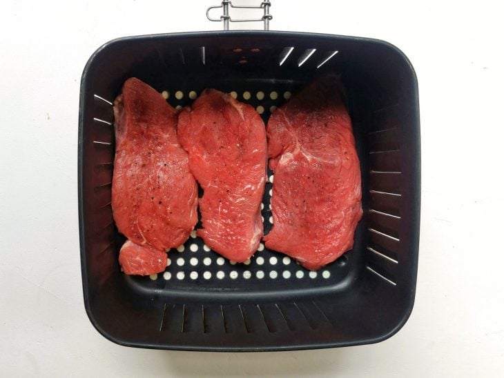 Bifes temperados dispostos dentro do cesto da airfryer.