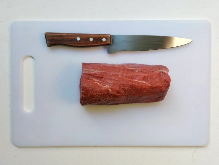 Uma tábua com uma peça de filé mignon e uma faca.