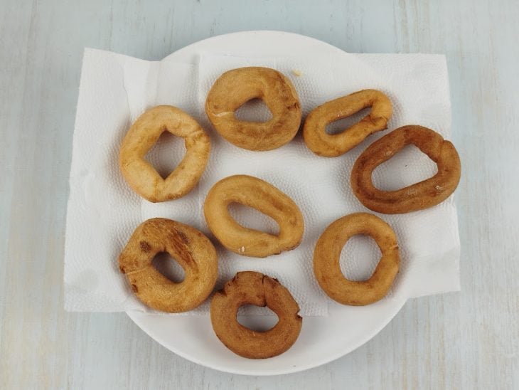 Rosquinhas sendo retiradas do óleo e colocadas sobre papel-toalha absorvente.